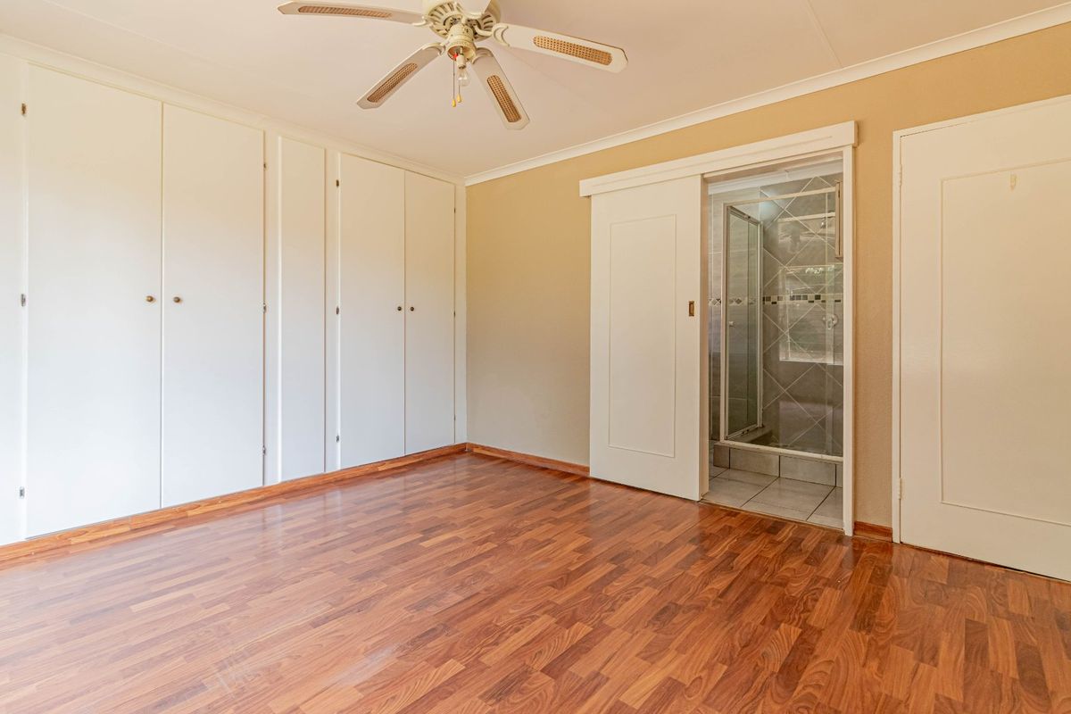 Bedroom featuring built-in cupboards, laminate flooring, a ceiling fan, and an en-suite bathroom accessed via a sliding door.