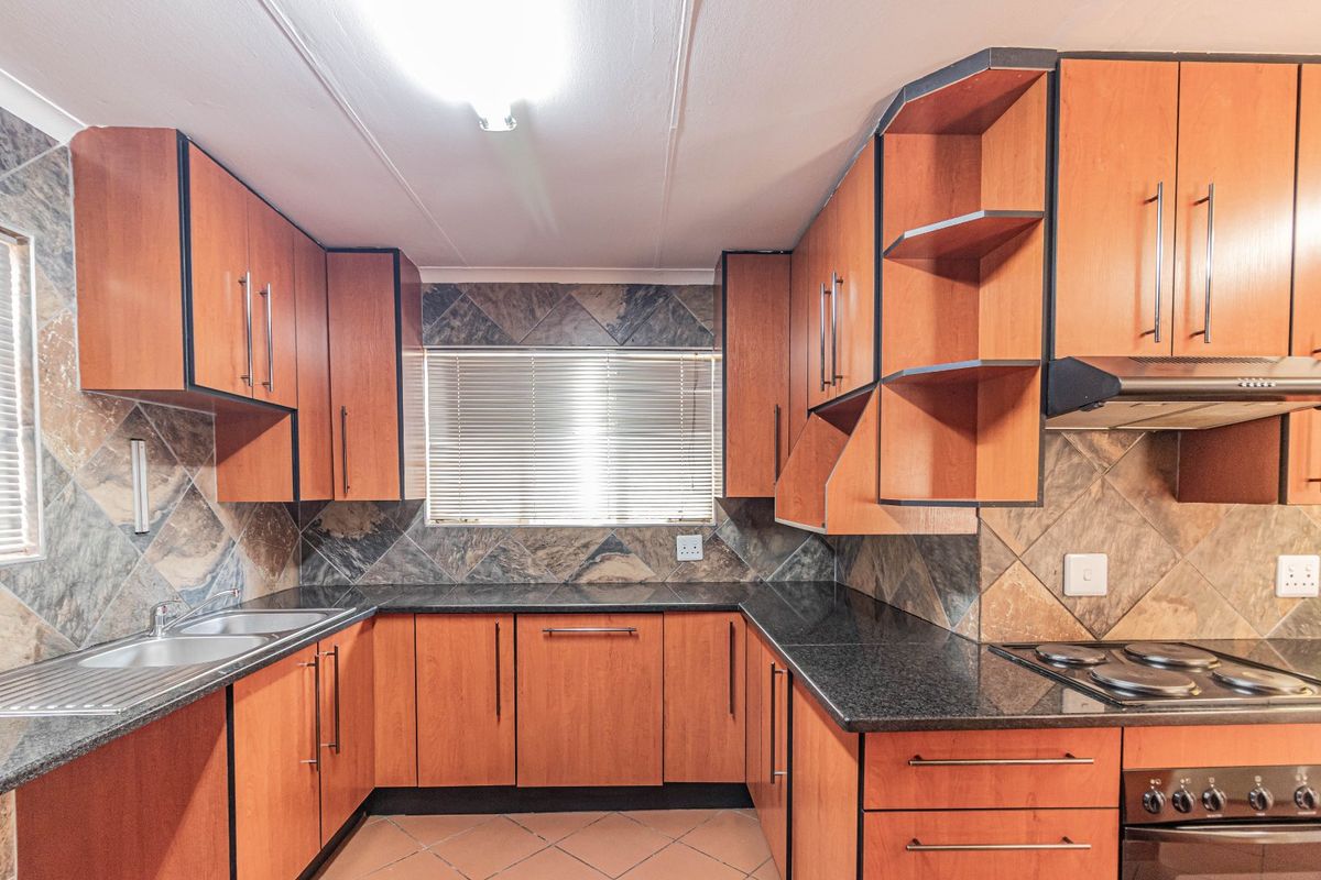 A functional kitchen featuring wood-finish cabinetry, dark granite countertops, a built-in oven and hob, and a tiled backsplash.