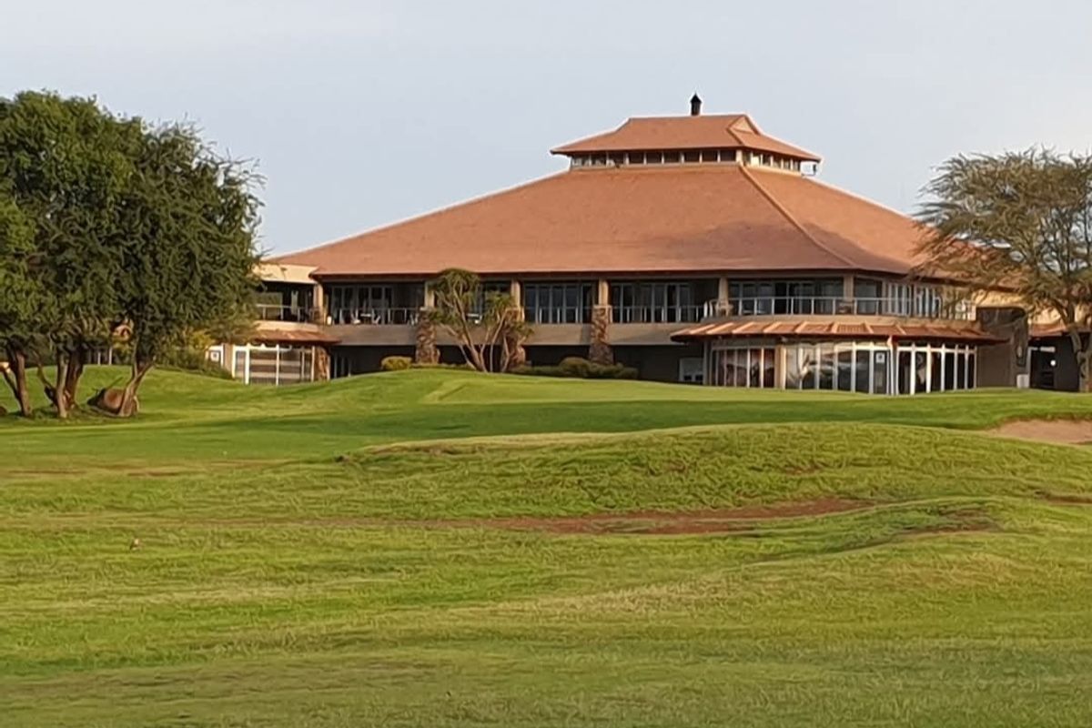 A view of a large clubhouse building situated on a well-maintained golf course, featuring a prominent tiled roof and extensive glass facade.