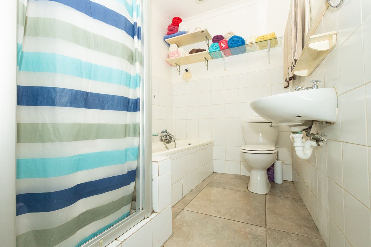 A functional bathroom featuring a built-in bathtub, wall-mounted basin, toilet, and tiled finishes throughout.