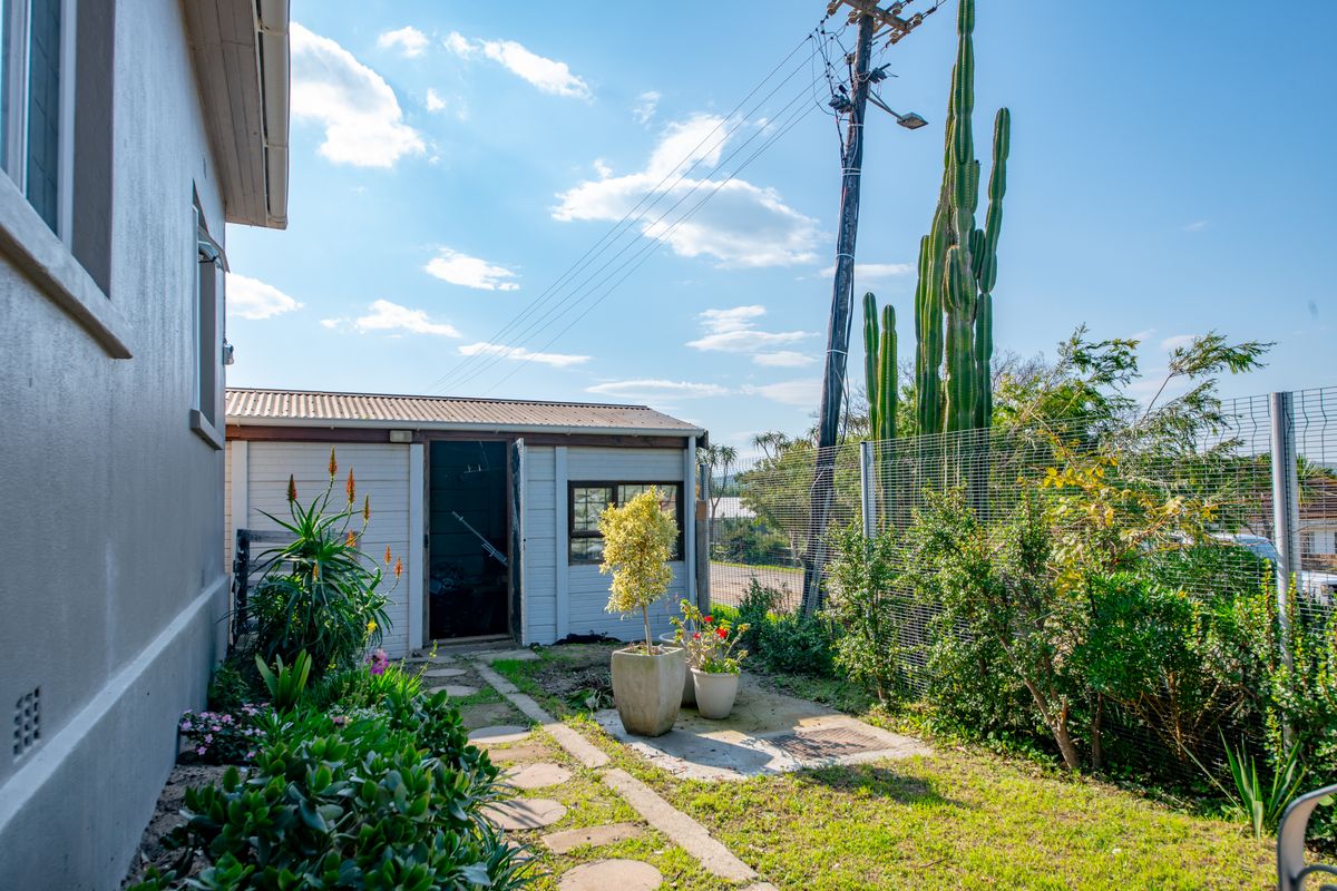 A rear garden area featuring a utility shed, stepping stone pathway, and established landscaping enclosed by mesh fencing.