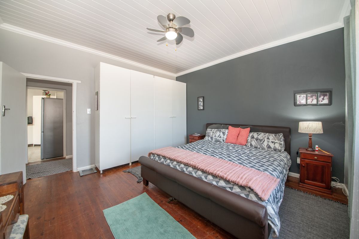 Spacious bedroom featuring polished timber flooring, a classic tongue and groove ceiling, a ceiling fan, and ample built-in cupboard storage.