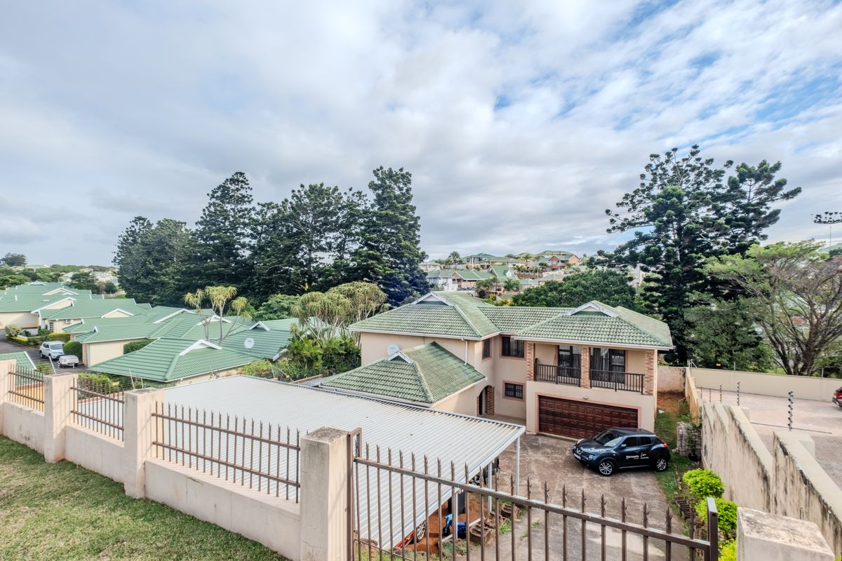 An elevated aerial view of a residential property featuring a tiled roof, balcony, garage, and secure perimeter fencing within a suburban estate setting.