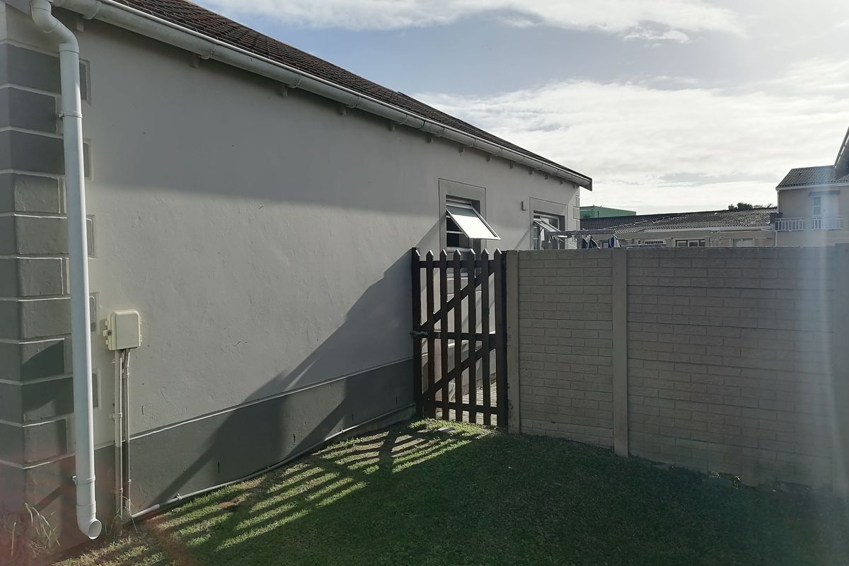 Rear exterior view of the townhouse featuring a small lawn, a secure timber gate, and a precast concrete boundary wall.