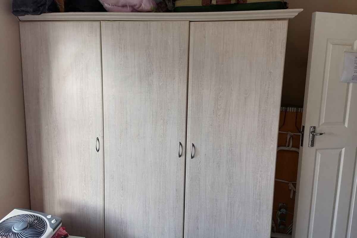 A bedroom featuring a light wood-grain finish built-in wardrobe with three doors.