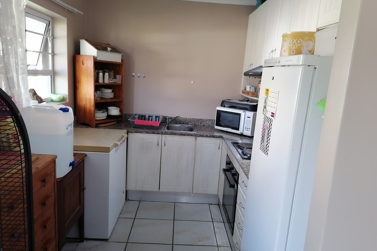 Compact kitchen featuring built-in cabinetry, granite countertops, integrated oven and hob, and tiled flooring. The space offers functional storage and preparation areas.