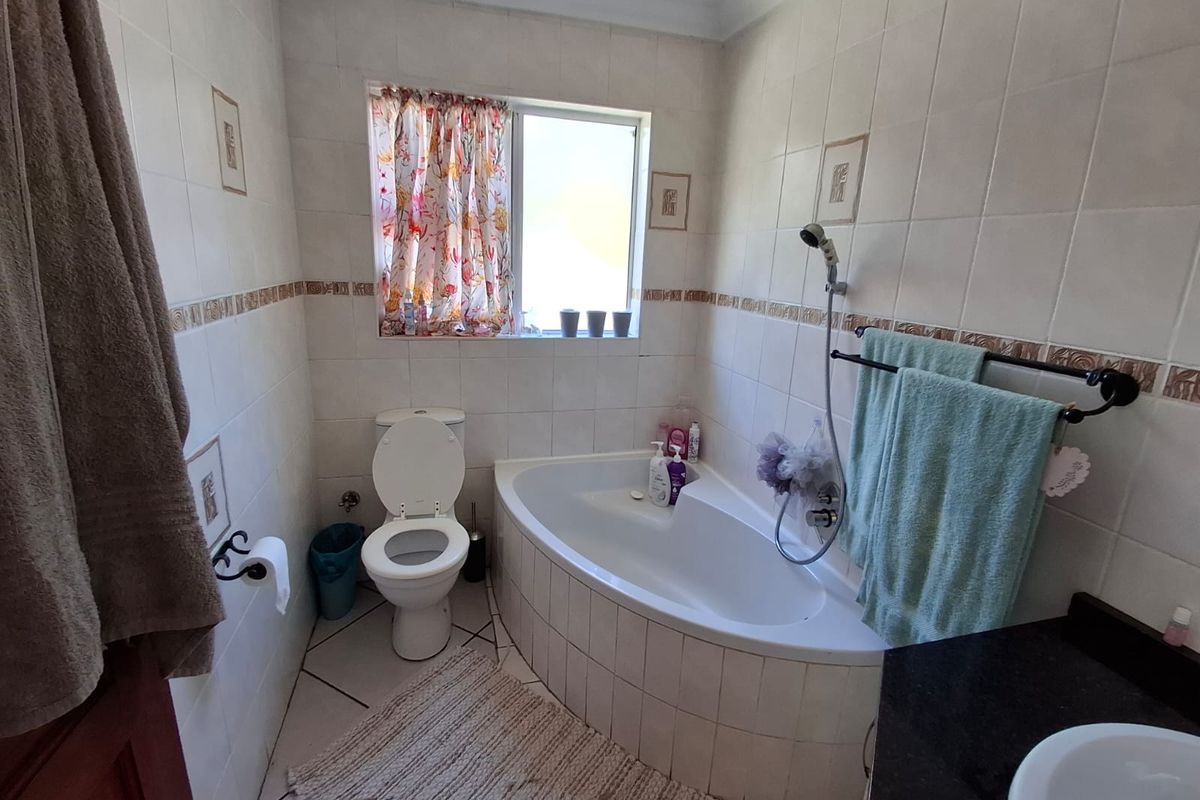 A functional bathroom featuring a corner bathtub with a handheld shower attachment, a standard toilet, and a vanity basin with a dark countertop.