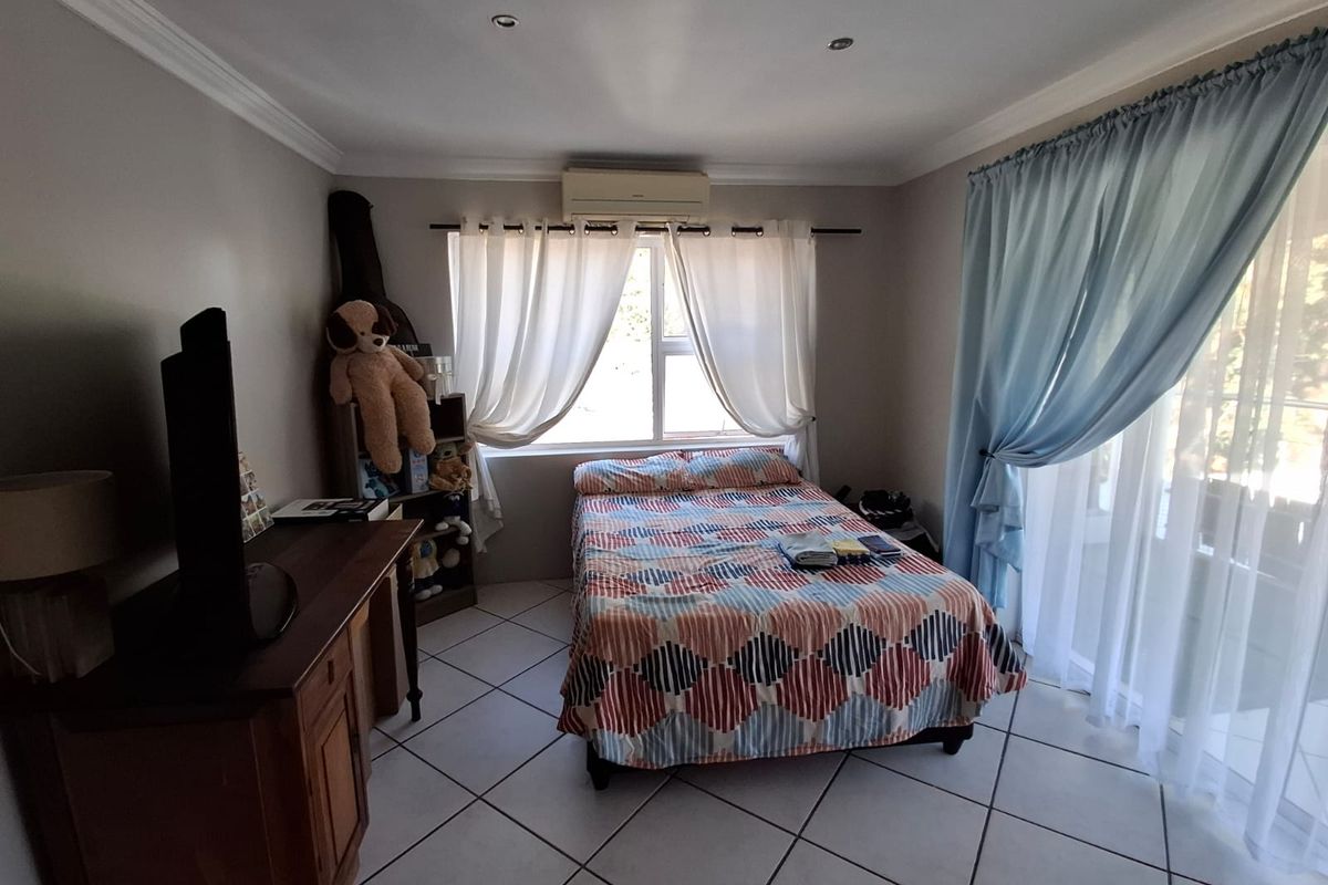 A bedroom featuring tiled flooring, recessed ceiling lighting, and a wall-mounted air conditioning unit, with access to an adjoining balcony through sliding glass doors.