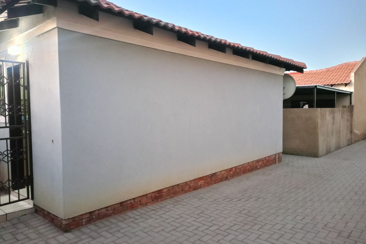 Side view of the property showing the exterior wall, terracotta roof tiles, brick plinth, and paved driveway area.