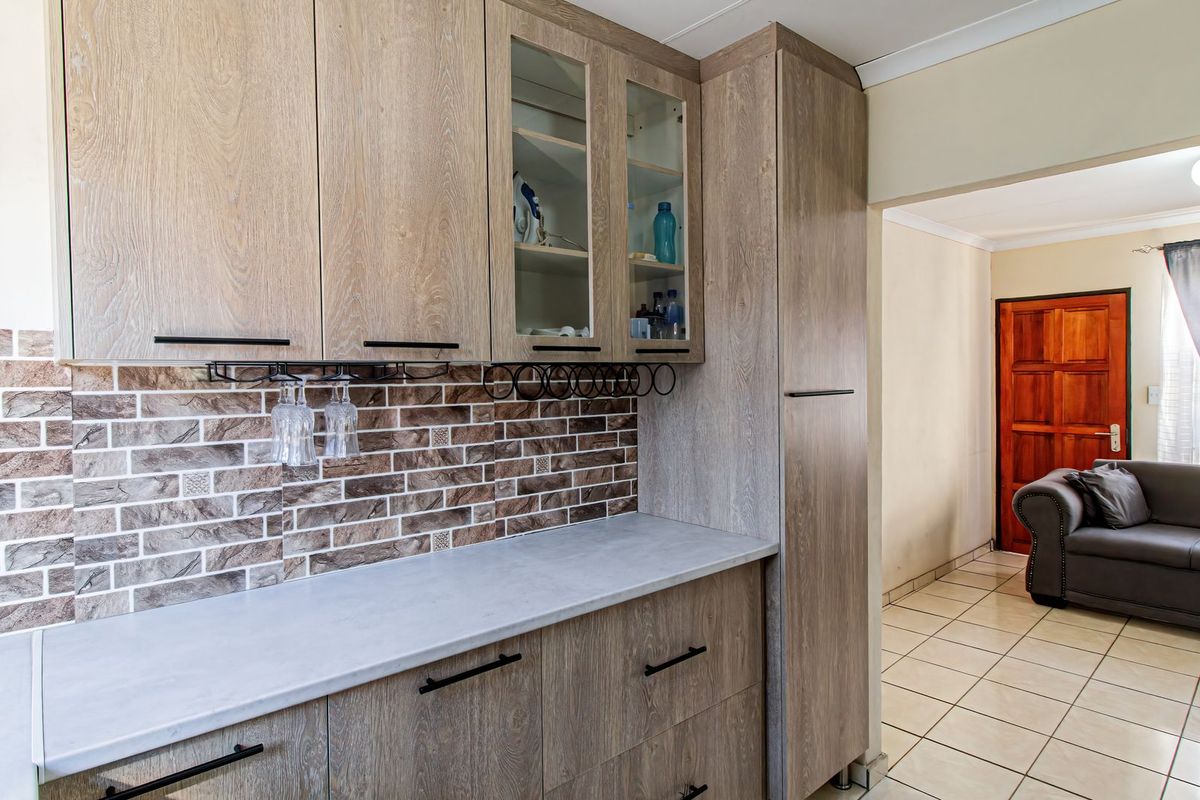 A well-maintained kitchen area featuring modern wood-look laminate cabinetry, a textured tile backsplash, and durable ceramic floor tiles leading into an adjacent living space.