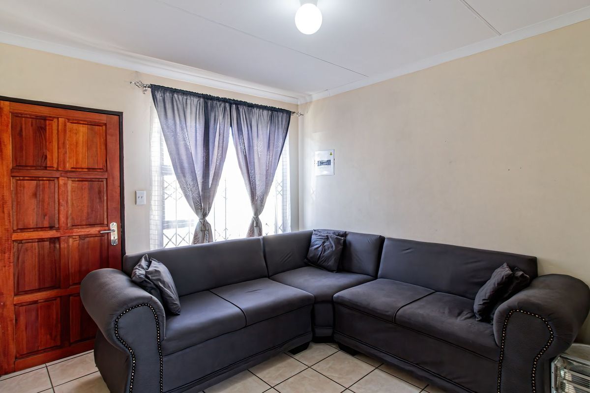 A living room featuring tiled flooring, a wooden entrance door, and a wall-mounted electrical distribution board.
