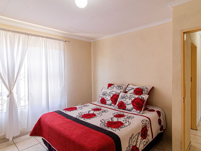 A functional bedroom featuring tiled flooring, neutral wall finishes, and a window fitted with a security gate.