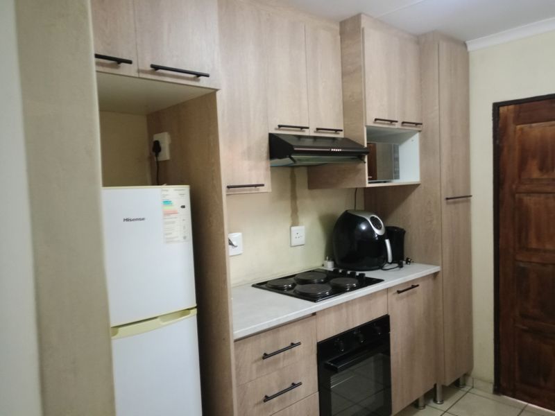 A compact kitchen featuring modern light wood-look cabinetry, integrated electric hob, built-in oven, extractor fan, and tiled flooring.
