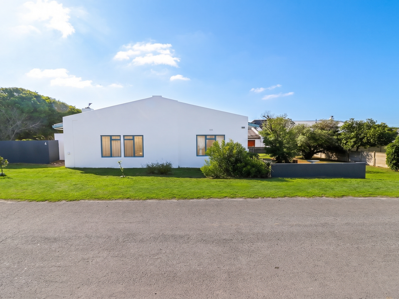 A clear front view of the property featuring a white facade, manicured lawn, and established garden elements.