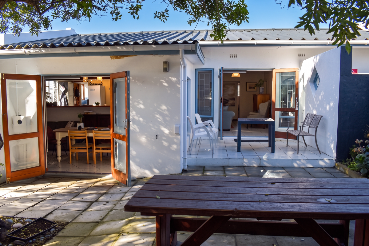 A rear exterior view of the house featuring a paved patio area with double door access to the interior living spaces.