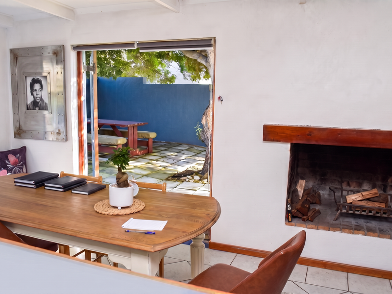 A living area featuring a built-in brick fireplace with a wooden mantel, tiled flooring, and direct access to an outdoor patio area.