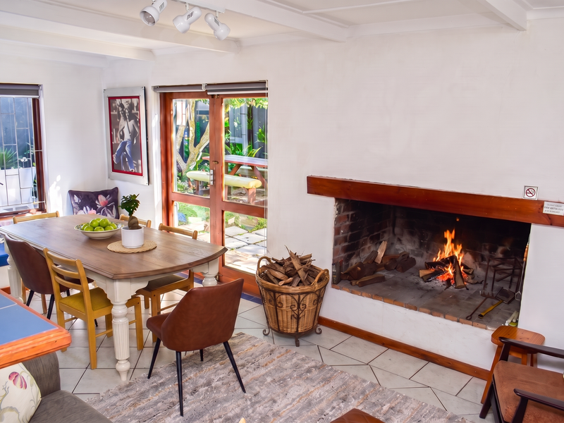 Open-plan living and dining area featuring a large built-in brick fireplace, tiled flooring, and direct access to the garden through wooden framed glass doors.