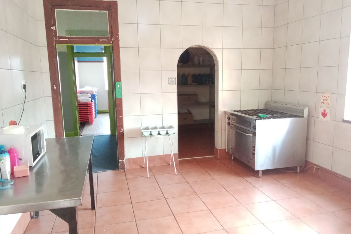 A functional kitchen area featuring tiled walls and flooring, a gas stove, and an arched pantry entrance, showing signs of dated finishes.