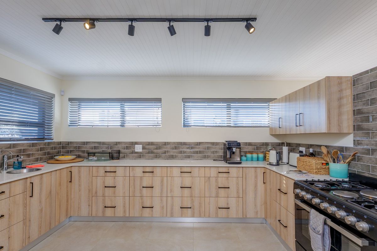 Modern kitchen featuring light wood-grain cabinetry, stone countertops, subway tile backsplash, and a professional-style gas range with overhead track lighting.
