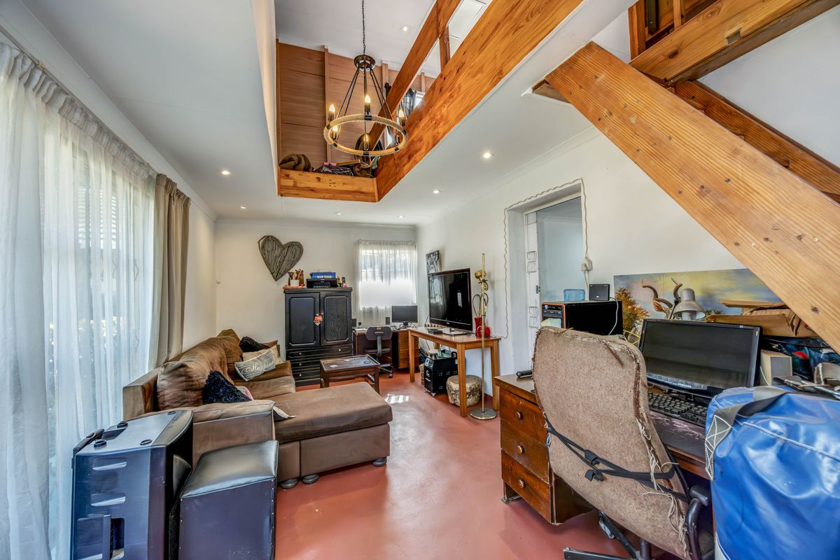 Living area featuring an exposed timber staircase leading to a mezzanine loft, recessed lighting, and painted concrete flooring.