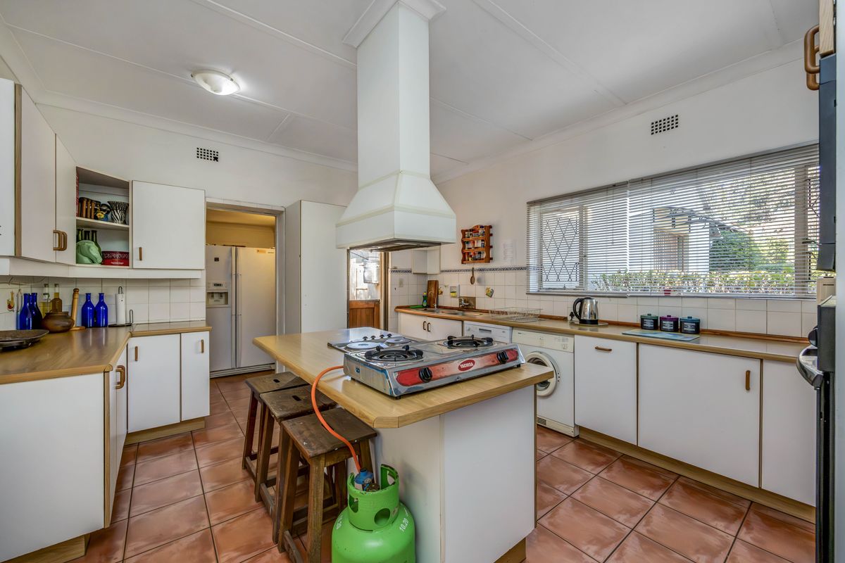 A functional kitchen featuring a central island with a gas cooktop, ample cabinetry, tiled flooring, and a tiled backsplash with a view to the exterior.