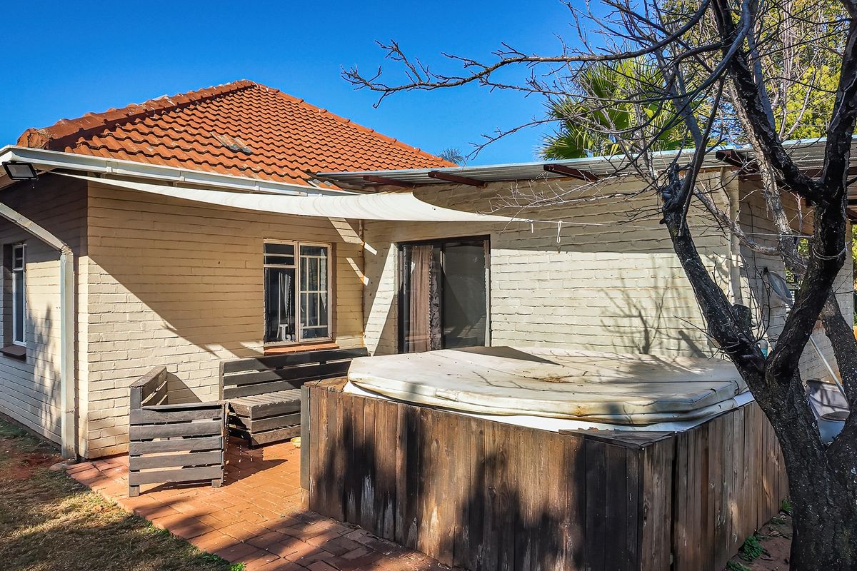 Rear exterior view of the house featuring a paved patio area, brick facade, and tiled roof with a shade sail installation.