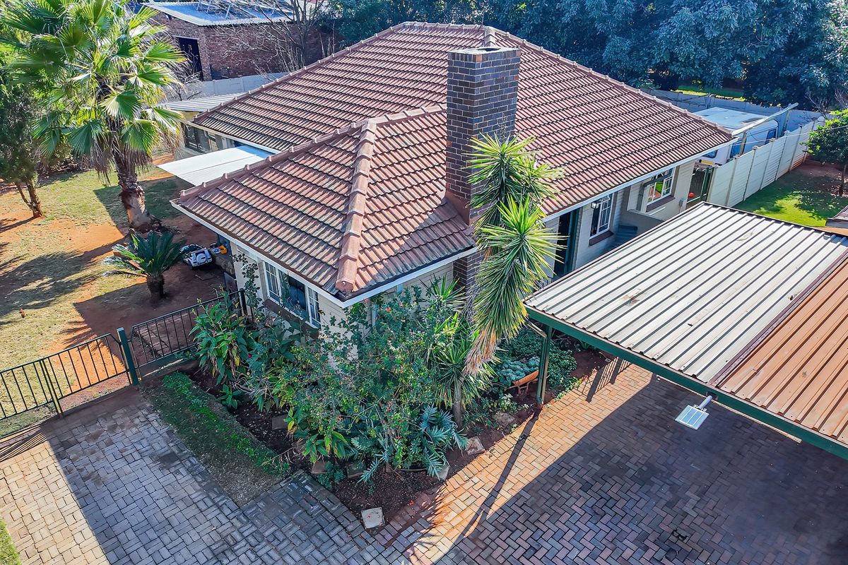 Aerial view of a residential property featuring a tiled roof, brick chimney, paved driveway, and a covered carport area.