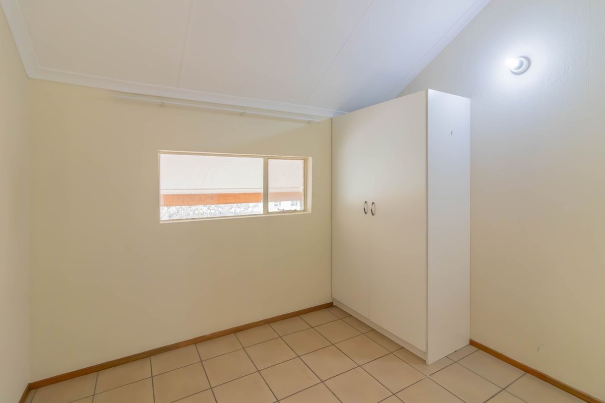 A clean, empty bedroom featuring neutral tiled flooring, a vaulted ceiling, and a built-in white wardrobe.
