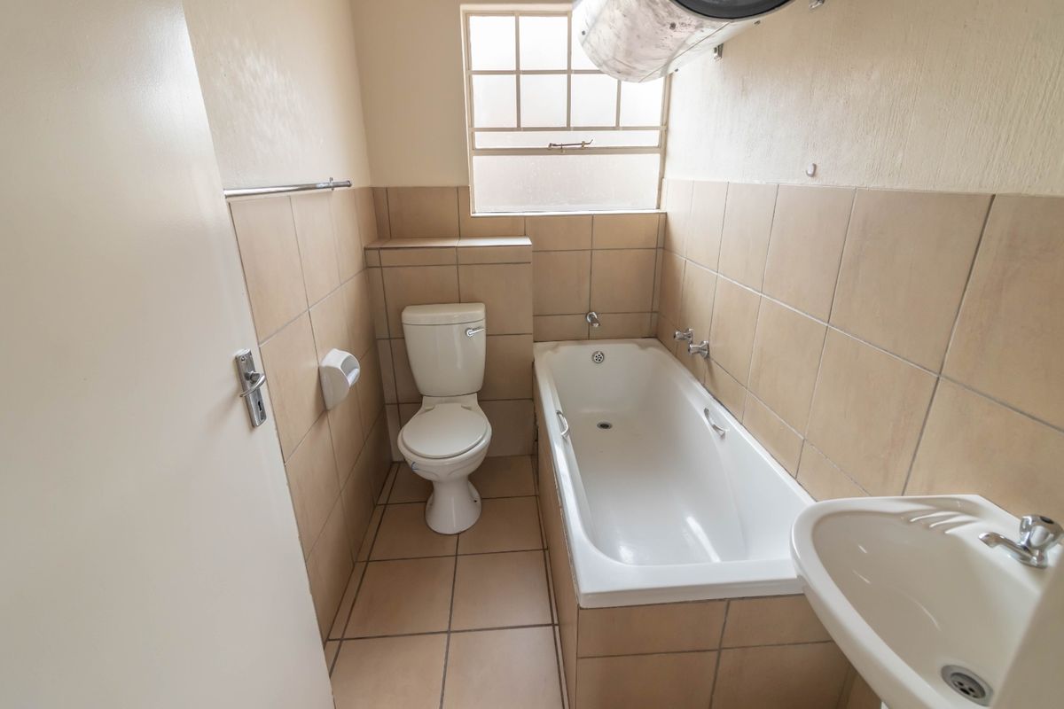 A functional bathroom featuring a bathtub, toilet, and washbasin with neutral wall and floor tiling.