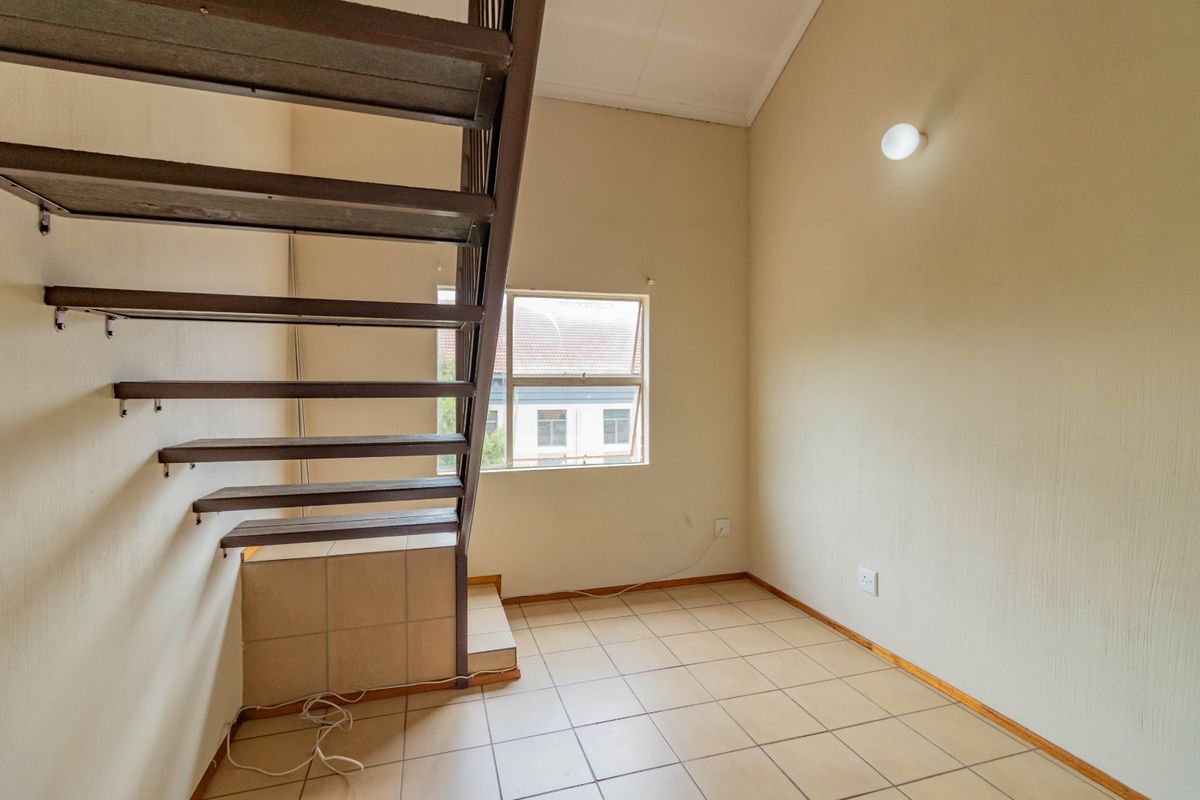 An empty living area featuring tiled flooring, a metal staircase, and a window, offering a blank canvas for interior design.