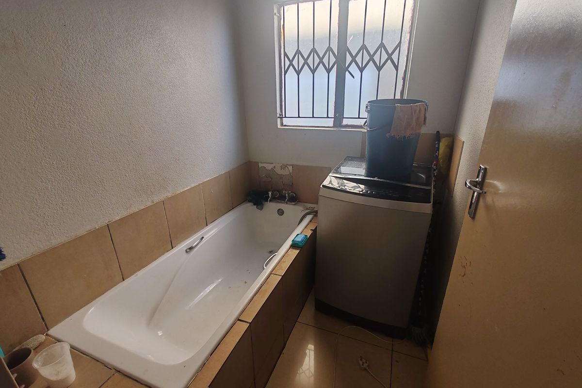 A functional bathroom featuring a built-in bathtub, tiled splashbacks, and a window with security bars, requiring some cosmetic updates to the wall finishes.