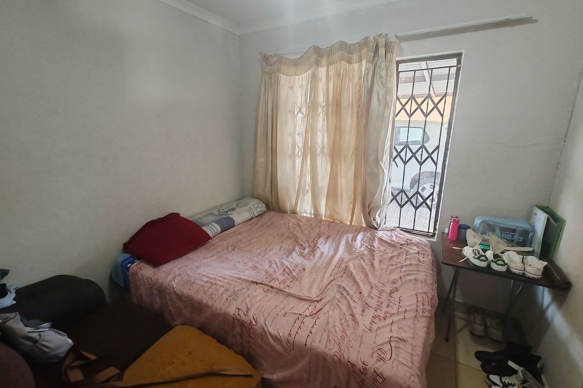 A functional bedroom featuring a window with security bars and a protective security gate, providing basic accommodation.