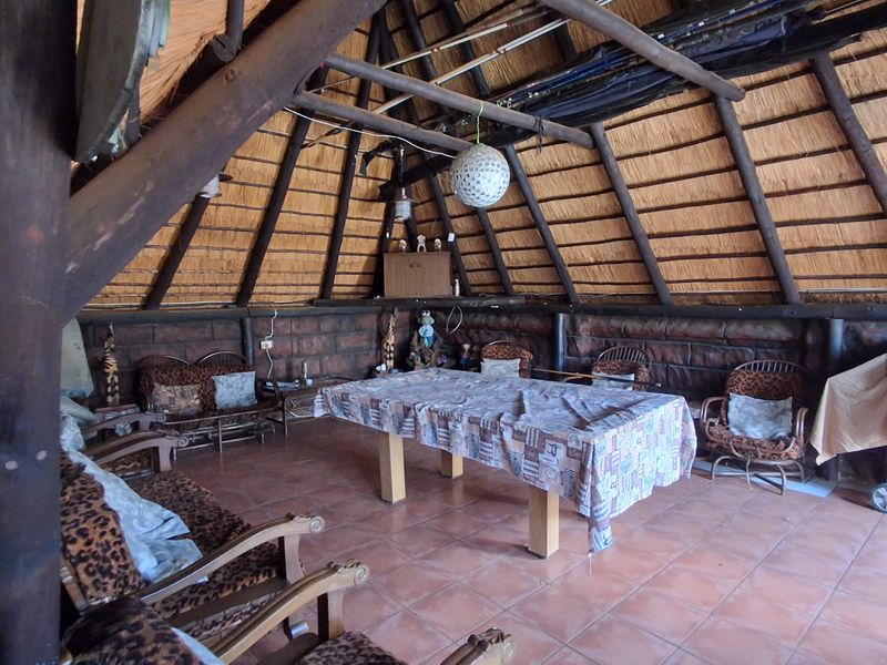 A rustic open-plan entertainment area featuring a traditional thatched roof, exposed timber trusses, and tiled flooring, ideal for casual outdoor gatherings.