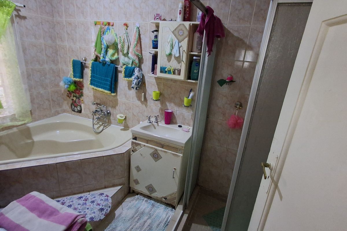 A compact bathroom featuring a corner bathtub, a small vanity with integrated sink, and a separate shower enclosure with tiled walls.
