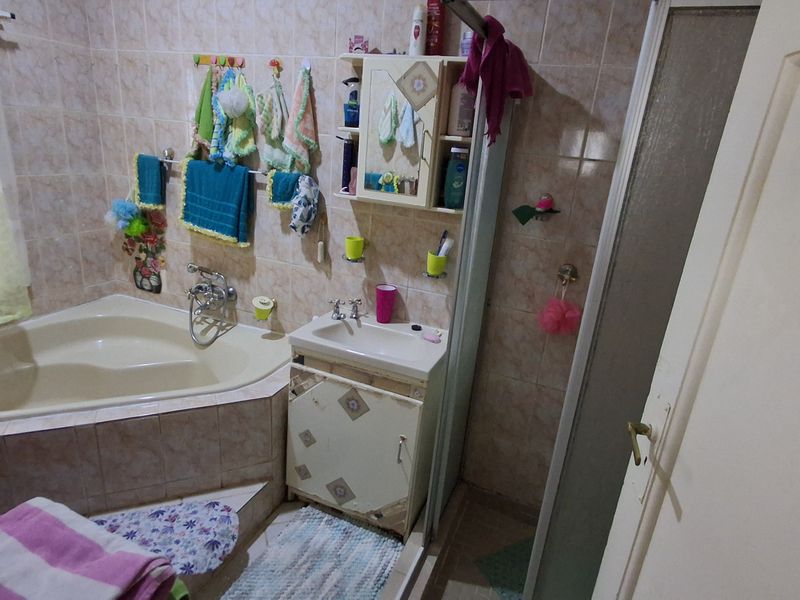 A compact bathroom featuring a corner bathtub, a small vanity with integrated sink, and a separate shower enclosure with tiled walls.