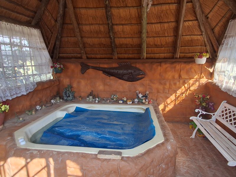A covered outdoor spa area featuring a built-in hot tub with a protective cover, set under a traditional thatched roof structure.