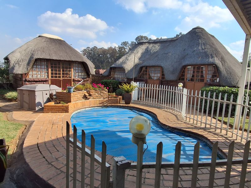 Outdoor pool area featuring a swimming pool with safety fencing, surrounded by brick paving and two traditional thatched-roof structures.
