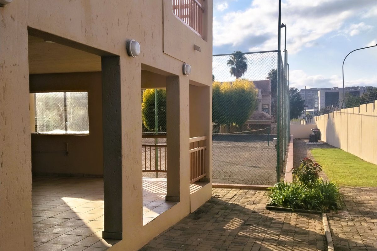 Exterior view of an apartment complex featuring a covered patio area, paved walkways, and an adjacent tennis court facility.