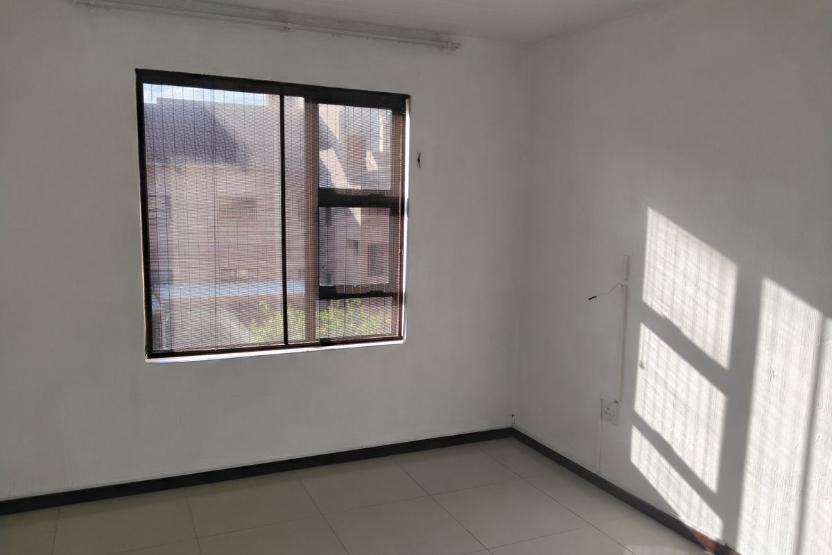 A bright, empty bedroom featuring neutral tiled flooring, clean white walls, and an aluminium-framed window with a fitted blind.