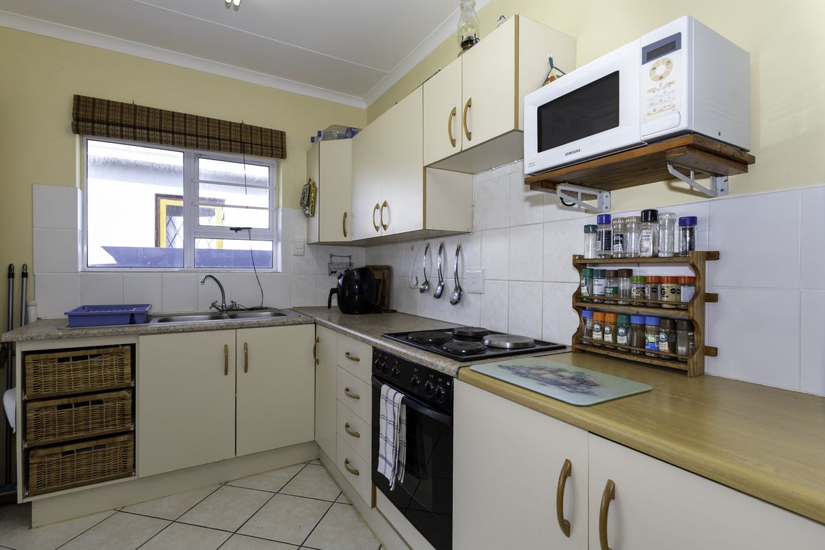 A functional kitchen featuring laminate countertops, built-in cabinetry, an electric hob with oven, and tiled flooring, offering a practical layout for daily meal preparation.