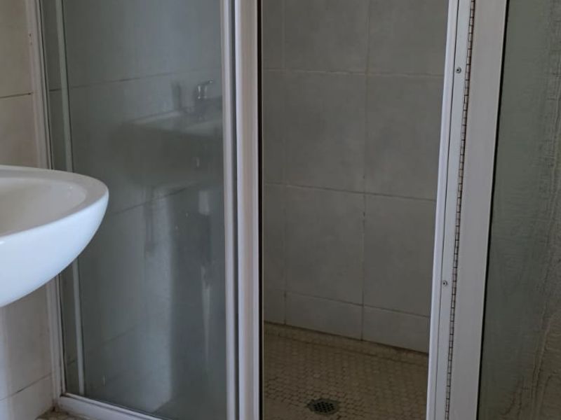 A functional bathroom featuring a shower enclosure with a sliding door and a pedestal basin, finished with neutral floor and wall tiling.