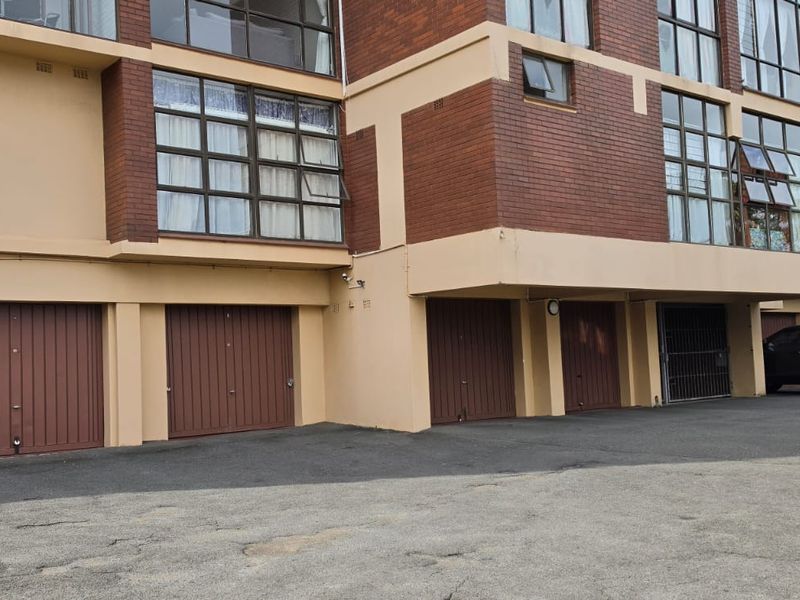 Exterior view of a multi-story apartment building featuring a brick facade, multiple garage units, and an asphalt driveway.