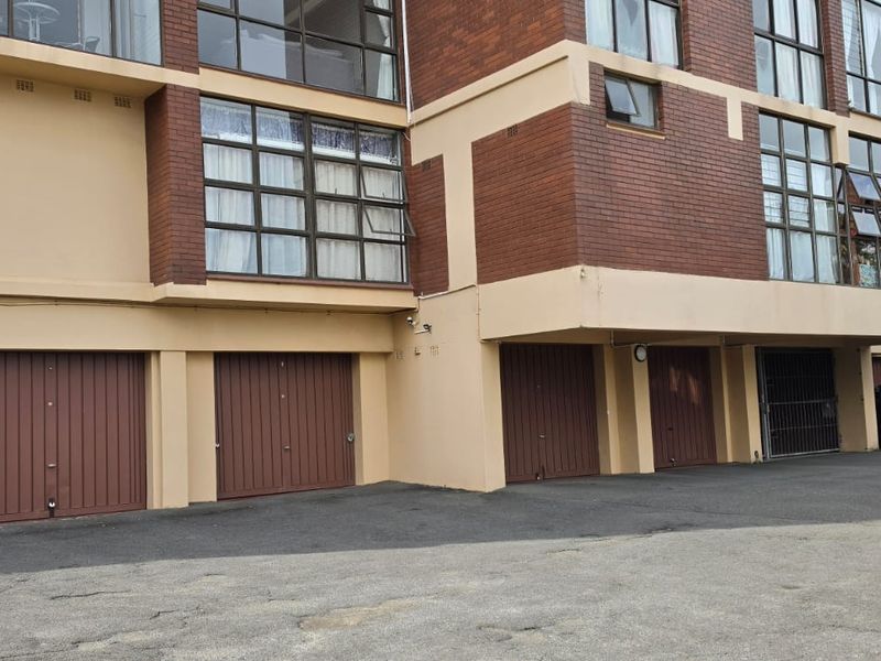 Exterior view of a multi-story flat building featuring a brick facade and a row of ground-level garage doors with an asphalt driveway.