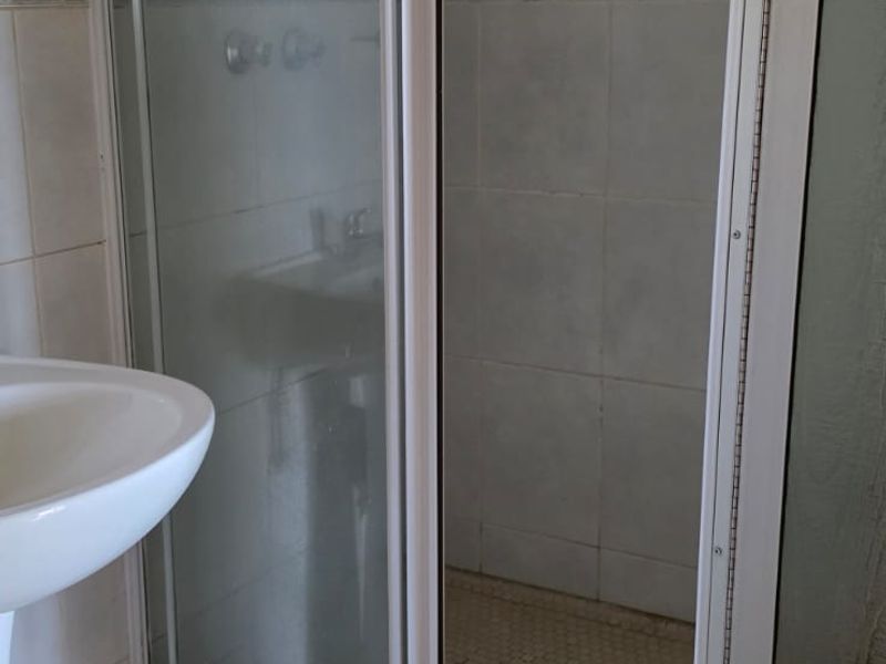 A functional bathroom featuring a shower enclosure with glass doors and a pedestal basin, finished with neutral wall and floor tiling.