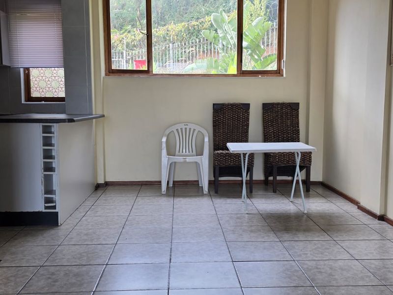 Open plan living area featuring tiled flooring and a breakfast bar, providing a functional space with natural light from large windows.