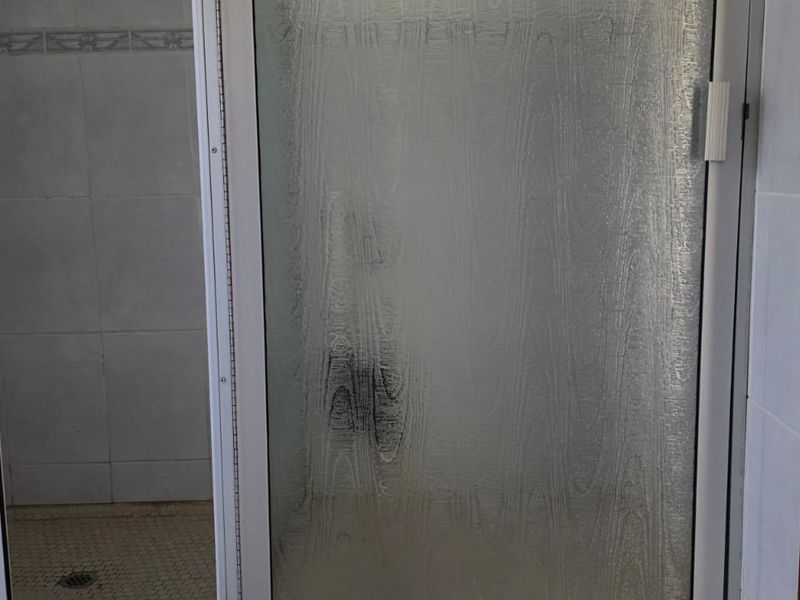 A functional bathroom shower area featuring a textured glass door, tiled walls, and mosaic floor tiling.