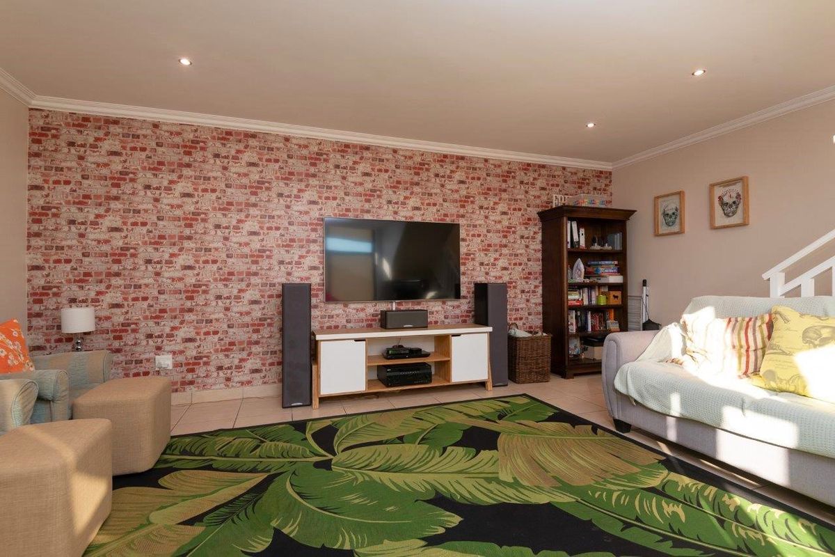 A comfortable living room featuring a decorative brick-effect feature wall, tiled flooring, and recessed ceiling downlights.