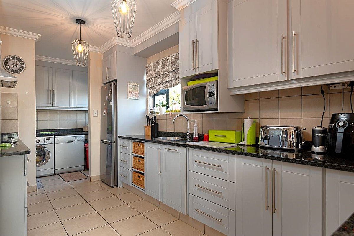 A well-maintained kitchen featuring light grey cabinetry, granite countertops, tiled backsplash, and an integrated laundry area with tiled flooring.