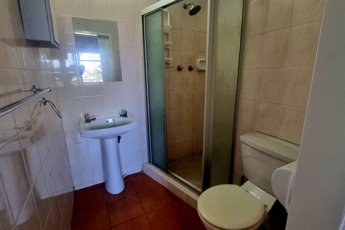 A dated bathroom featuring a pedestal basin, a shower cubicle with a sliding door, and a standard toilet with tiled walls and flooring.