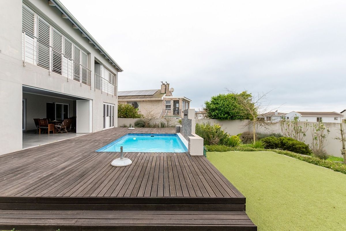 Rear exterior view featuring a timber deck, swimming pool with water feature, and a landscaped garden area adjacent to the main house.